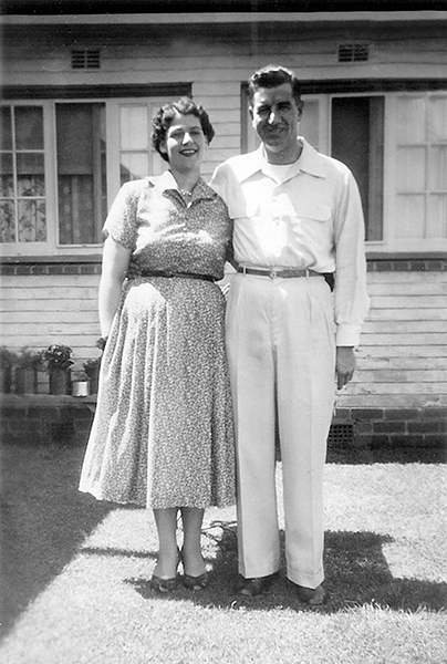 Old black and white picture showing two newly weds in front of new home.
